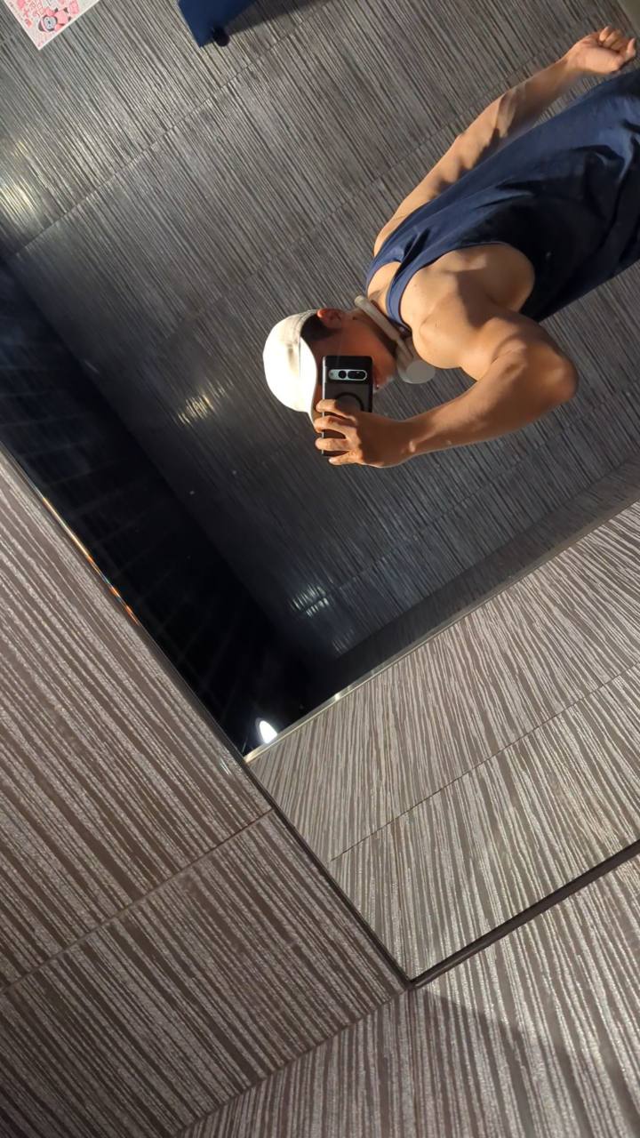 Foto cermin Aris di gym, memakai topi putih, headphone, dan atasan olahraga biru gelap.