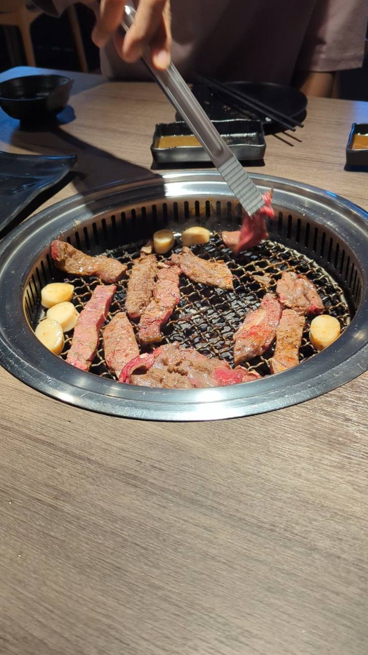 Panggangan bundar di meja makan, berisi potongan daging dan dilengkapi penjepit logam.
